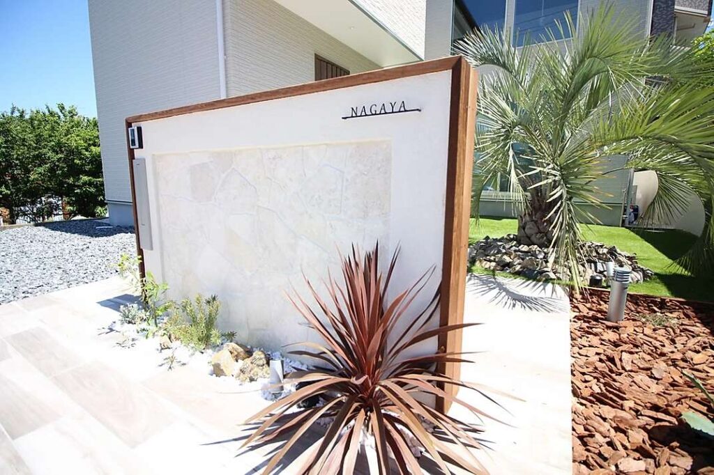 リゾート感のある洋風オシャレ外構。白い門柱とウッドチップを組み合わせた植栽で高級感の演出。